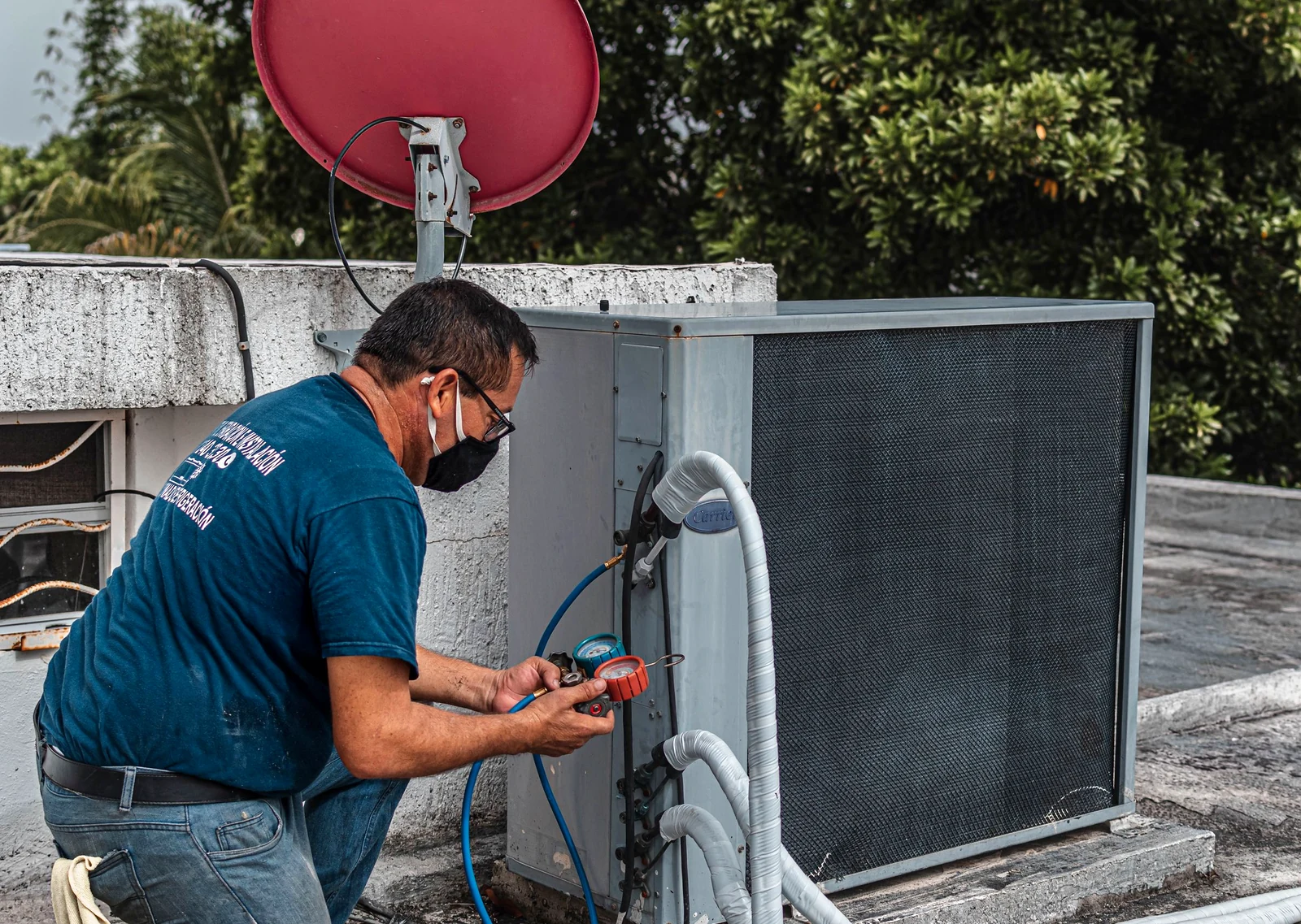 Technician checking refrigerant gauges on a rooftop cooling unit